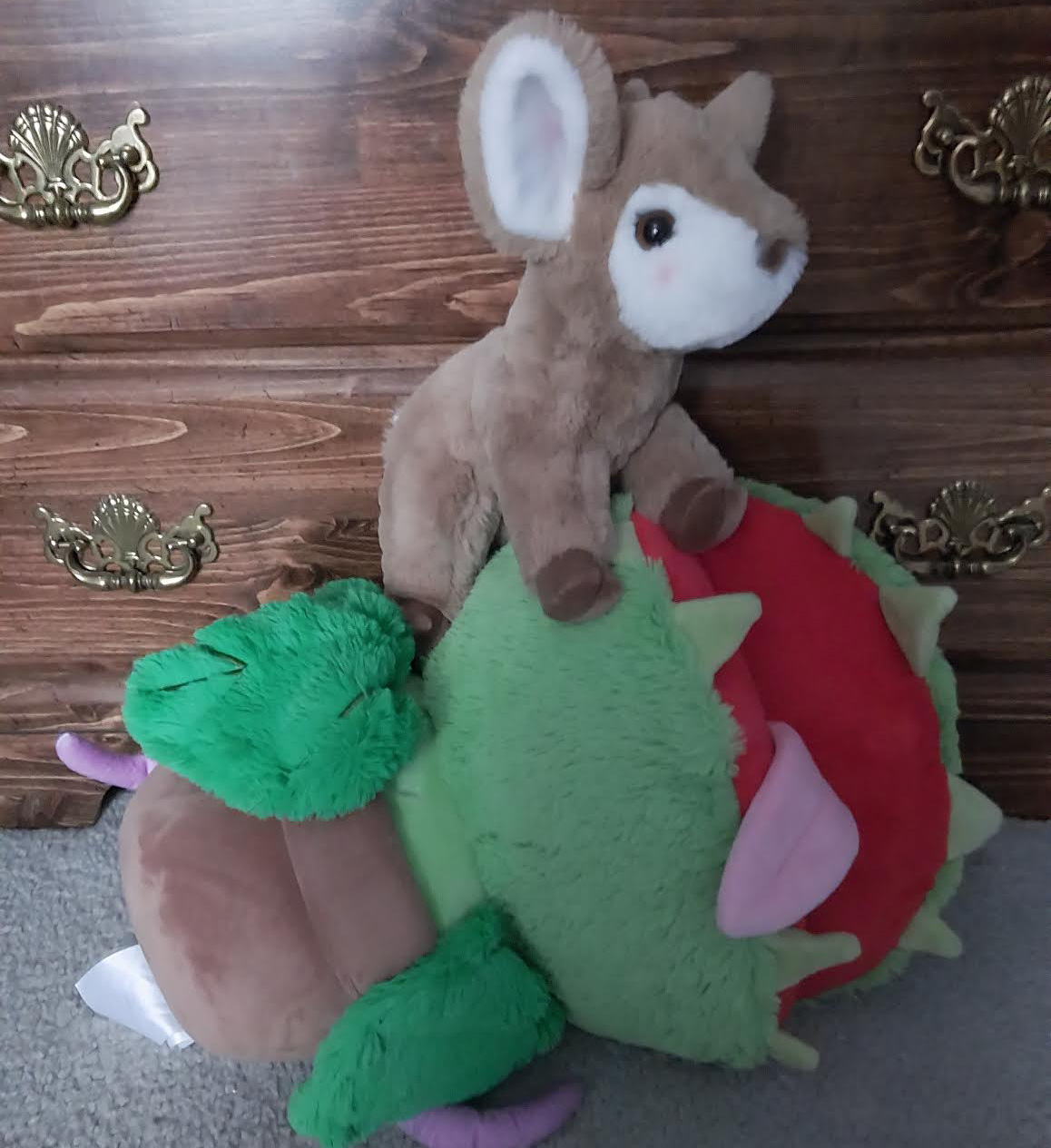 Arin, a soft tan deer plush, stands atop Twoey, a plush potted plant who resembles Audrey II from the musical Little Shop of Horrors. Twoey’s tongue is stuck out as if she has been defeated.